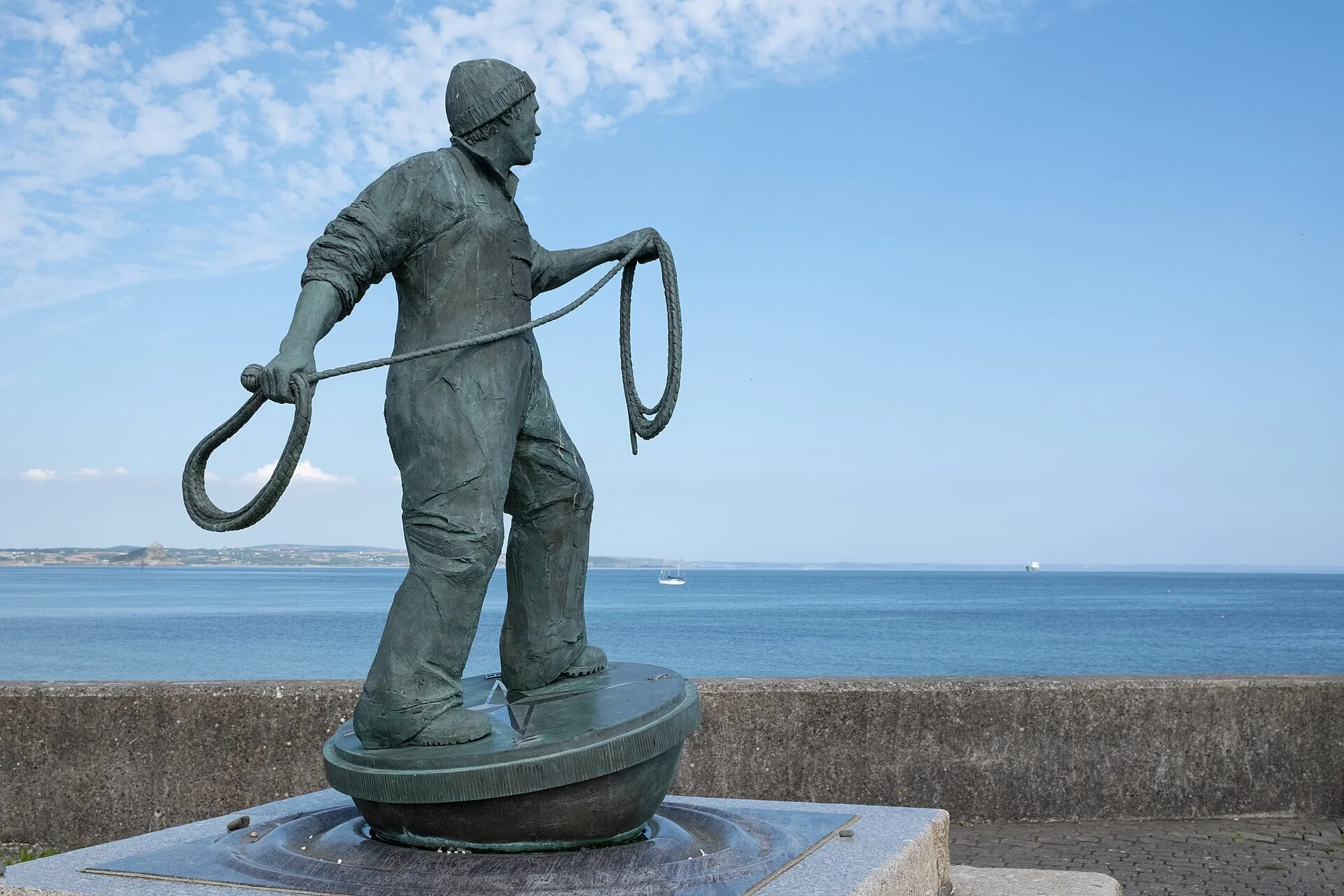 The bronze Newlyn fisherman statue holding a coiled rope, with the sea behind