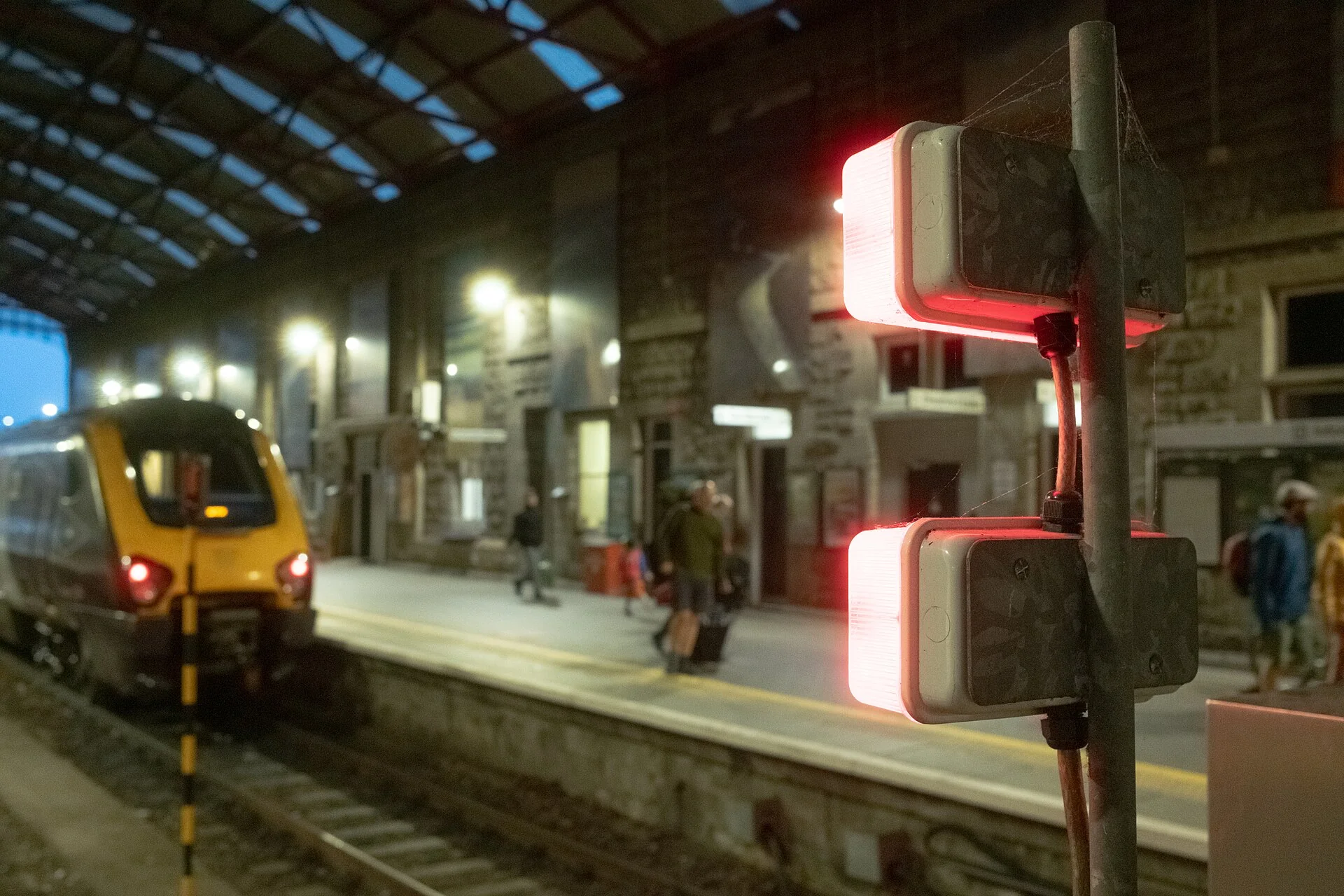 A train at a platform under the roof of Penzance station, with red signal lamps in the foreground
