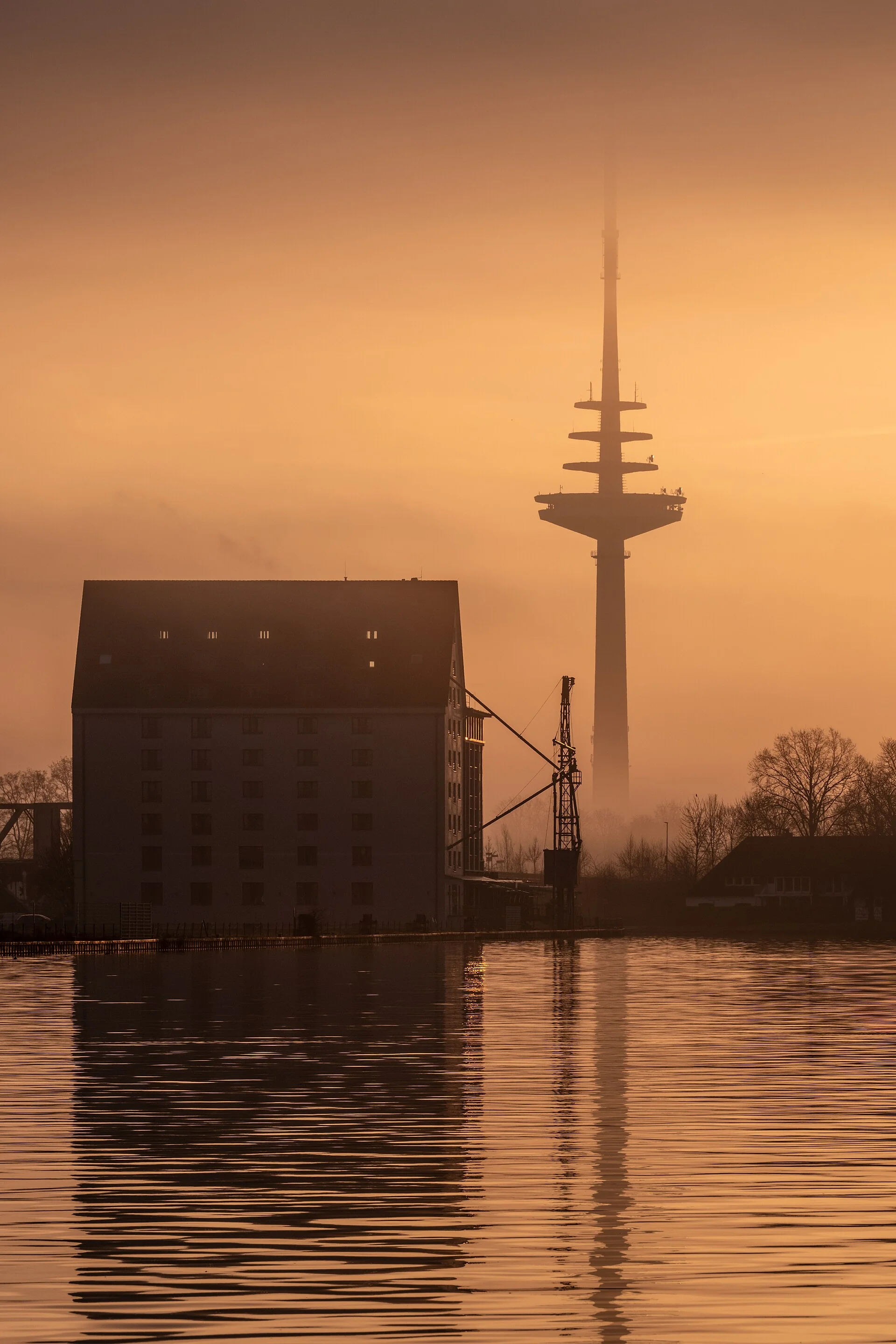 A harbour warehouse and a telecom tower in Münster against an orange sky