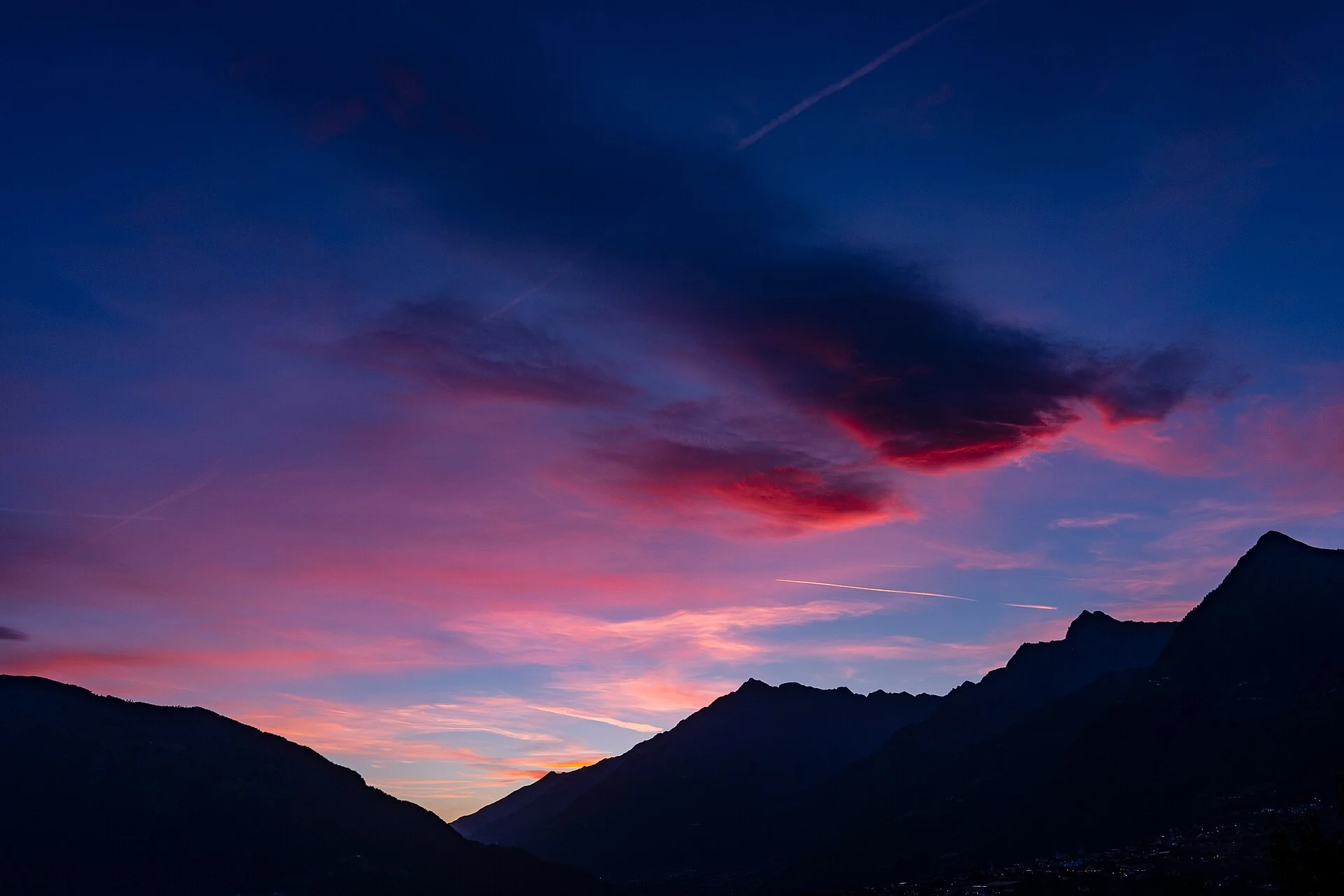 Mountains in silhouette under a pink and blue dusk sky over Schenna