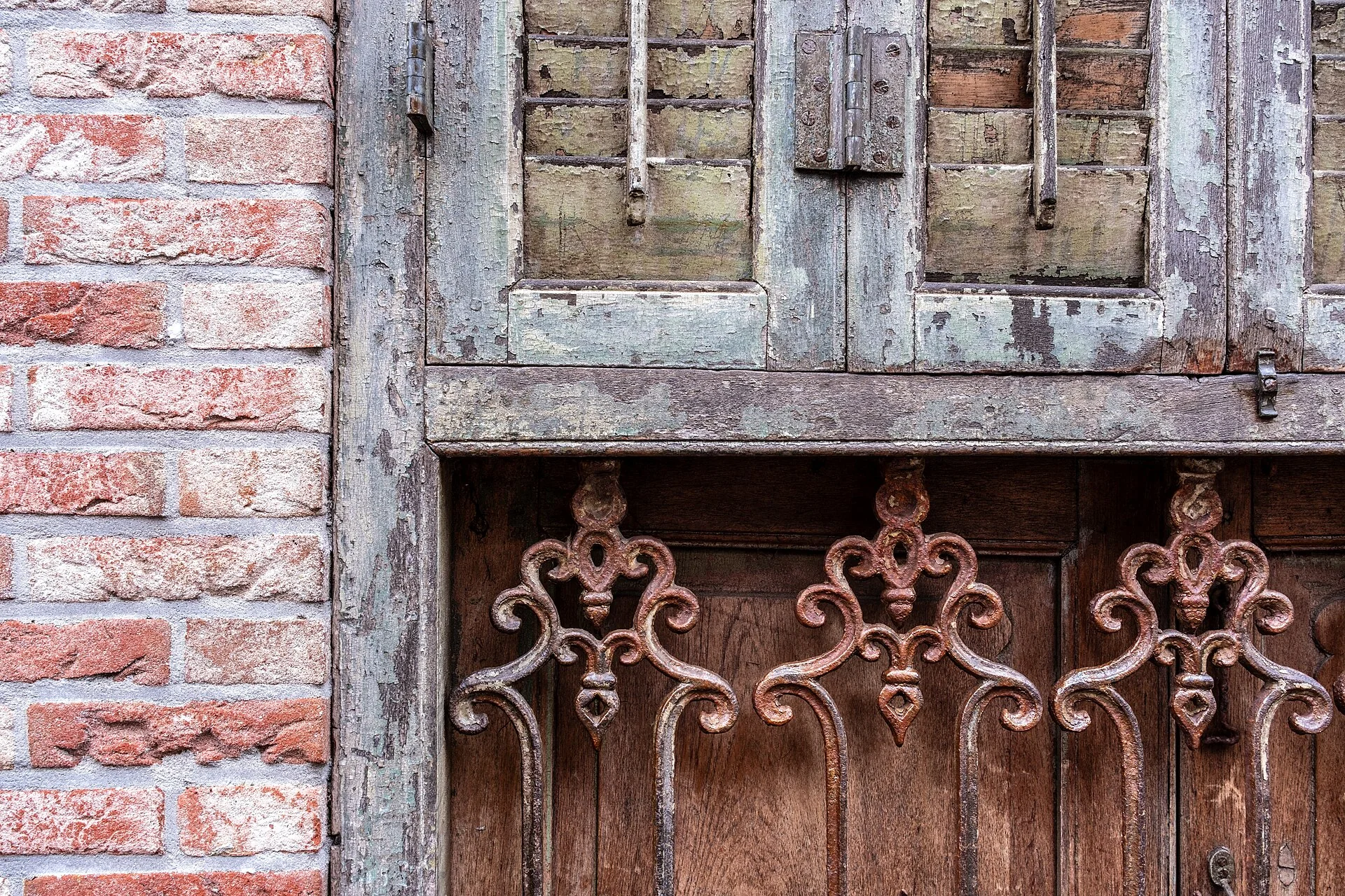 Weathered wooden shutters with ornate iron fittings in a brick wall in Den Burg
