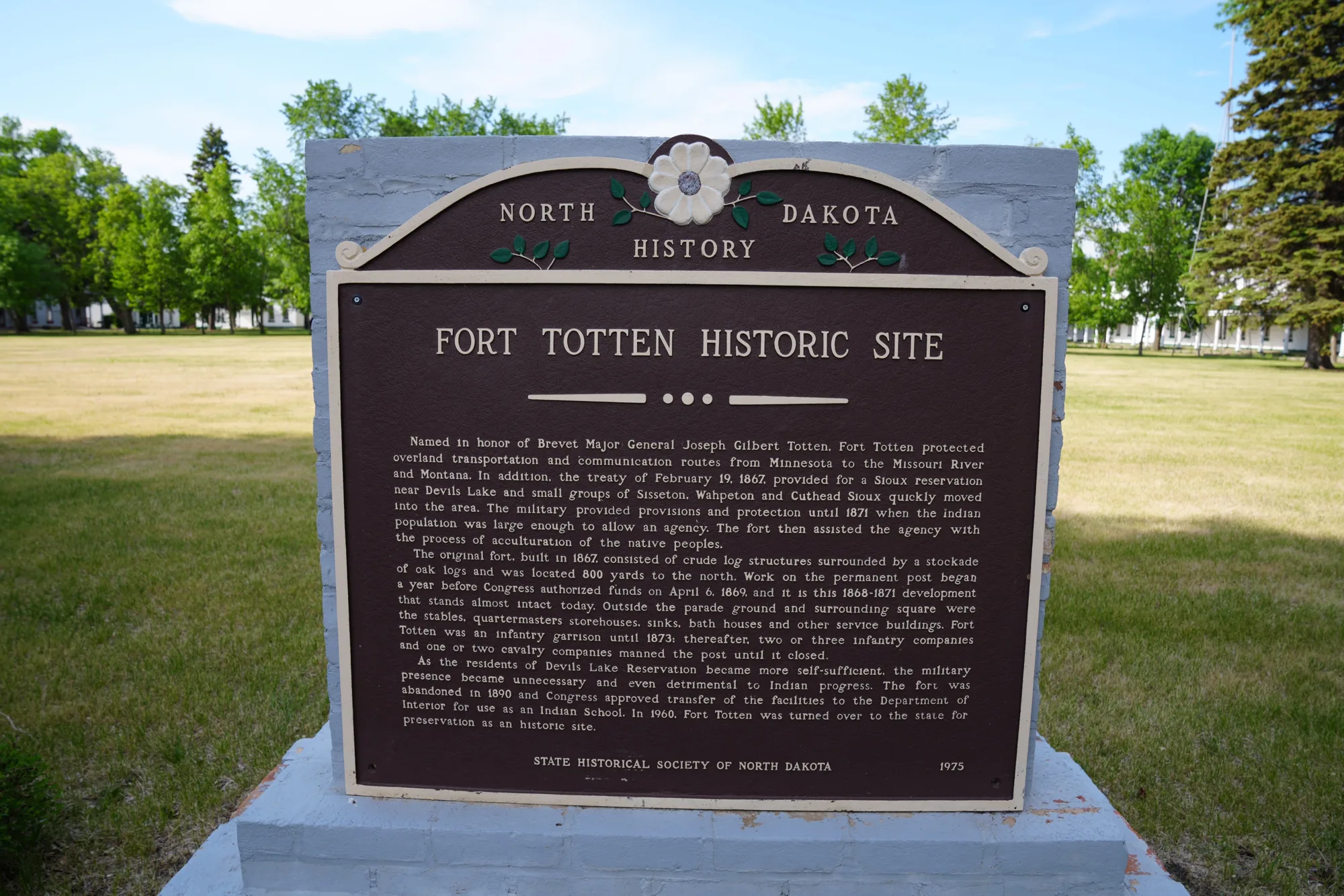 A brown historic-site marker sign on a lawn in front of trees