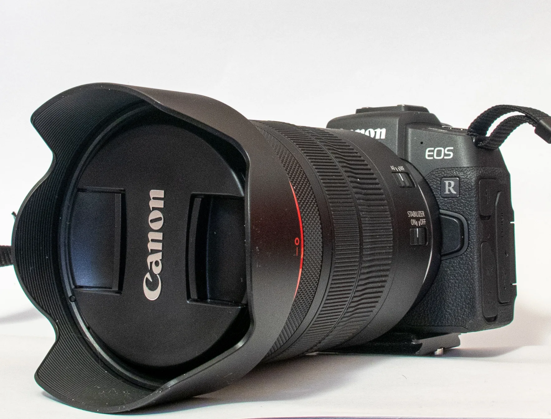 A black Canon EOS RP with a large RF 24-105mm F4 L zoom lens and hood on a white background