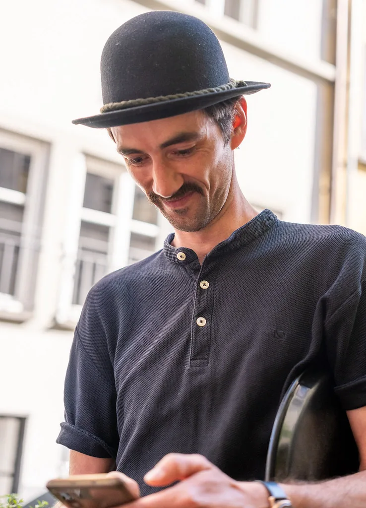 A man in a bowler hat with a phone on the street