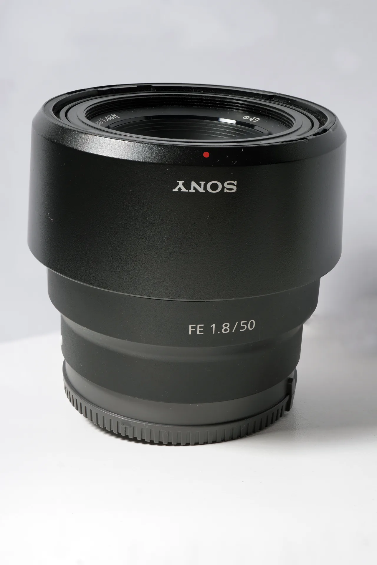 Sony FE 50mm F1.8 lens standing upright on a white surface, with FE 1.8/50 printed on the barrel